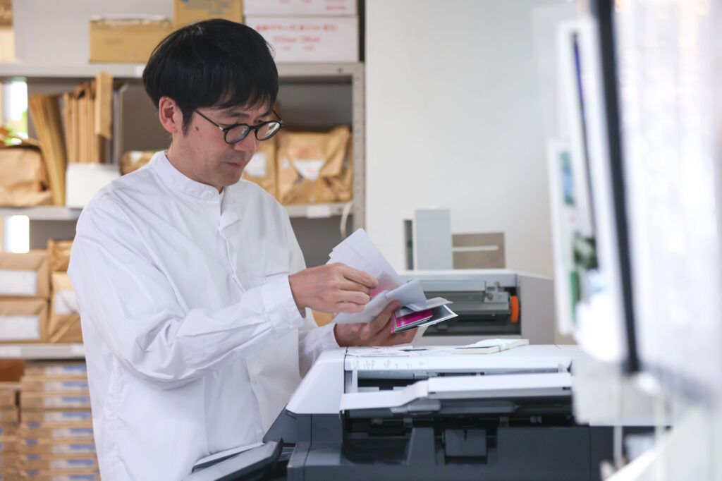 印刷機の前で色見本を見て確認しているスタッフ